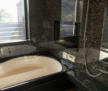 Marble-clad bathroom with built-in bathtub, wall-mounted shower, mirror and window at Mayu Futahari in Shizuoka