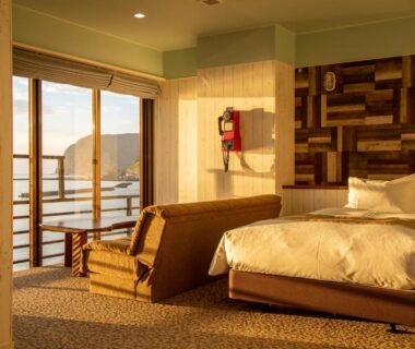 Sunlit room with bed, sofa and sliding balcony doors at Meijikan, Shizuoka