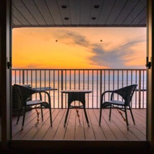 Wooden balcony with two chairs and small table overlooking calm ocean at sunset from Meijikan in Shizuoka