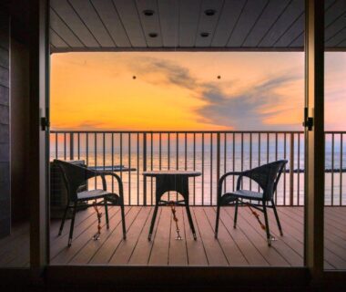 Wooden balcony with two chairs and small table overlooking calm ocean at sunset from Meijikan in Shizuoka