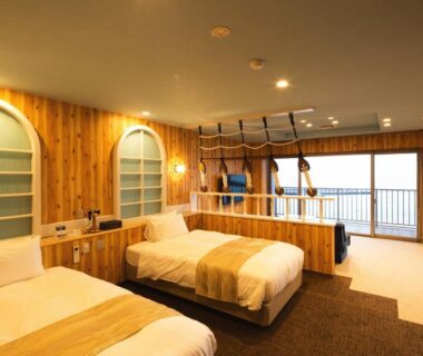 Two single beds in a wood-paneled Meijikan room with balcony doors and pendant lighting in Shizuoka