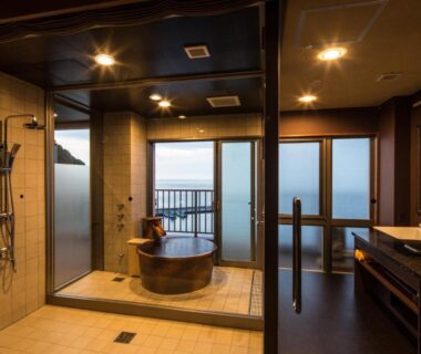 Indoor bathing area with wooden tub, shower and balcony overlooking the sea at Meijikan, Shizuoka