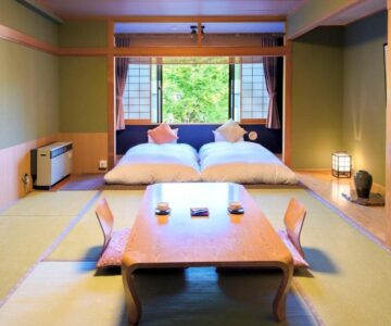 Tatami room with low wooden table, futon bedding, shoji screens and greenery visible through window at Meitoya So in Yamagata