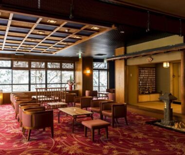 Spacious ryokan lounge with chairs, low tables, tatami alcove and large windows overlooking trees