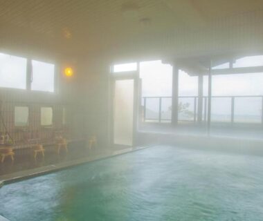 Steam-filled indoor onsen with bathing stools, shower stations and large windows at Michishio in Mie