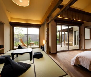Tatami mats with low table, futon cushions and bed beside shoji doors opening to a garden at Migiwaya, Shizuoka