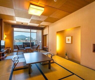 Traditional tatami room with low table and sliding doors opening to balcony with coastal and mountain views at Migiwaya, Shizuoka