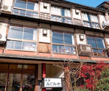 Three story wooden ryokan exterior with shoji style windows, entrance sign and potted plants at Migumiya Ryokan Hyōgo Kansai