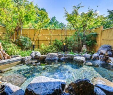 Rock-lined outdoor onsen with bamboo fence and lush garden setting at Mikasa in Nara