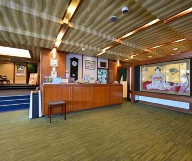 Spacious ryokan reception with wooden ceiling, check-in counter, seating area and decorative artwork at Mimatsukan, Gunma, Kantō