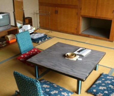 Tatami room with low table, floor cushions, small TV and wooden storage cabinet at Mimatsuso Ryokan, Hokkaidō