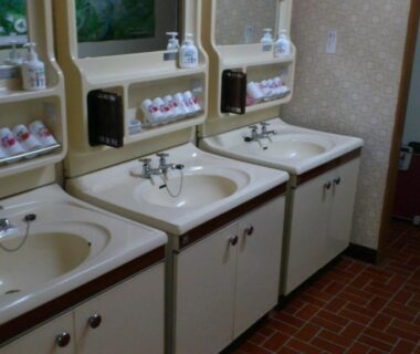Three-sink communal wash area with mirrors, soap dispensers and tiled floor at Mimatsuso Ryokan in Hokkaidō