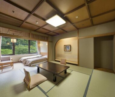 Traditional tatami room with low table, zabuton cushions and twin beds overlooking garden at Minakami Hotel Juraku, Gunma
