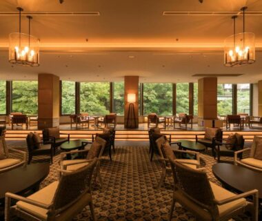 Warm wood-furnished lounge with armchairs and low tables overlooking verdant forest through wide windows at Minakami Hotel Juraku Gunma