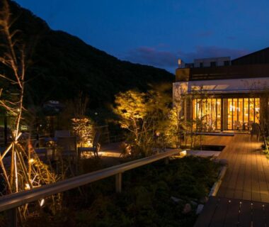 Nighttime wooden deck and illuminated garden beside glass facade with mountain silhouette, Minakami Hotel Juraku, Gunma