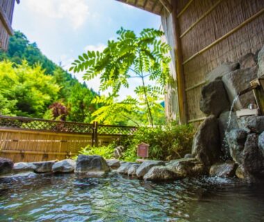 Outdoor rock-lined onsen under wooden shelter with bamboo fence and lush greenery at Minakamisansou in Gunma Kantō