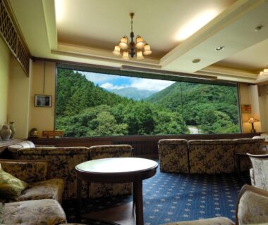 Sofa seating and tables facing a large window with green mountain view at Minakamisansou, Gunma
