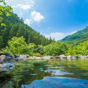 Rock-lined outdoor hot spring pool surrounded by green mountains and blue sky in Gunma