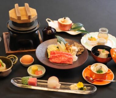 Assorted Japanese dishes on black table with lacquerware, ceramic bowls, and a small lidded pot