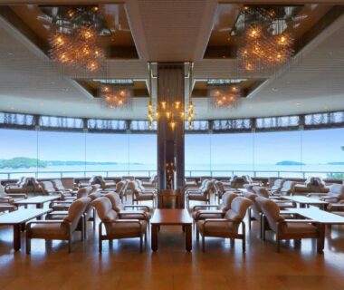 Spacious lounge with sofas, wooden flooring and panoramic windows overlooking the waterfront in Minami Sanriku Miyagi