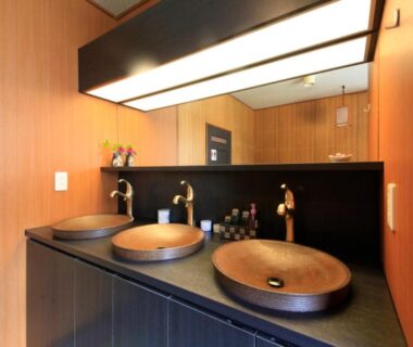 Three wooden vessel sinks on dark counter with backlit mirror in Minshuku Fukufuji washroom, Tochigi Kantō
