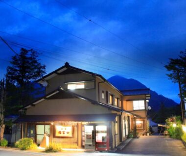 Lit traditional minshuku exterior and entrance at dusk with mountain backdrop, Minshuku Fukufuji, Tochigi
