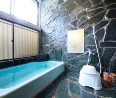 Stone-tiled bathing area with blue tub, shower stool and toiletries at Minshuku Fukufuji, Tochigi