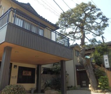 Two-story ryokan entrance with balcony and pine tree at Minshuku Ginmatsu in Ishikawa prefecture