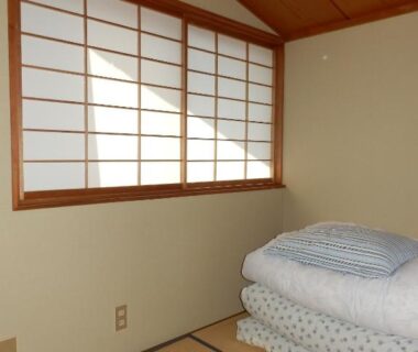 Tatami room with stacked futons and shoji window at Minshuku Ginmatsu in Ishikawa