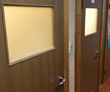 Wooden corridor with two restroom doors and frosted windows at Minshuku Iwatakan in Gifu