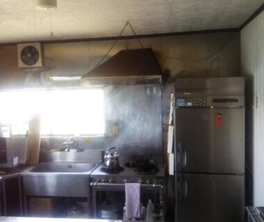 Shared kitchen with stainless counters stove and refrigerator at Minshuku Kamagari in Hiroshima