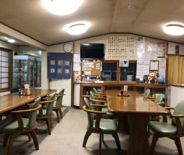 Dining room with wooden tables, green chairs, service counter and menu board at Minshuku Kawarabi-so in Nara