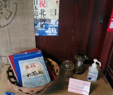 Brochures and hand sanitizer on wooden shelf near shoji door at Minshuku Kitamaebune, Ishikawa