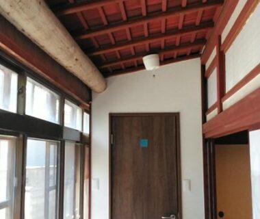 Sunlit wooden corridor with exposed beams, glass-panel windows and a wooden interior door at Minshuku Kitamaebune, Ishikawa