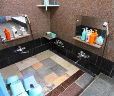 Tiled communal shower area with low stools, faucets, mirrors and toiletries at Minshuku Kobayashi, Yamanashi