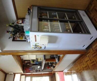 Beverage refrigerator in a cozy Minshuku common area with wooden flooring and shelving