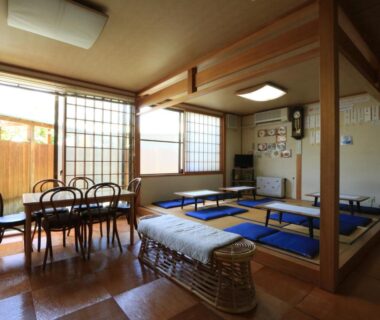Tatami room with low tables, shoji screens, dining chairs and a woven bench at Minshuku Miyama, Nagano