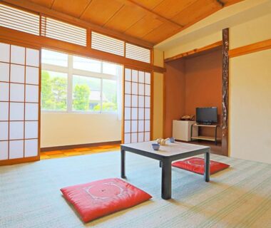Tatami room with low wooden table, red zabuton cushions, shoji screens and outside greenery visible through window