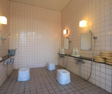Communal tiled washing area at Minshuku Miyama in Nagano with stools, handheld showers, mirrors and wooden buckets