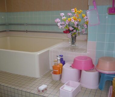 Tiled bathing room with deep tub, washing stools, buckets and flower vase at Minshuku Mutsukari Hokkaidō