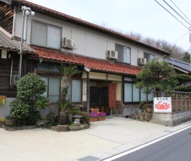Street-facing wooden ryokan with tiled roof, potted plants and traditional entrance at Minshuku Oe, Kyoto