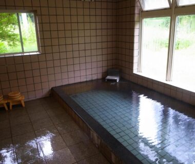 Small indoor tiled onsen bath with low wooden stools and green garden view through windows at Minshuku Takizawa Gifu