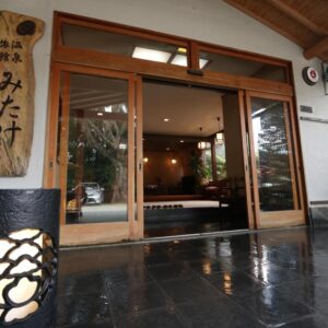 Polished stone entry with wooden sliding doors and Mitake signboard at a Kanagawa ryokan