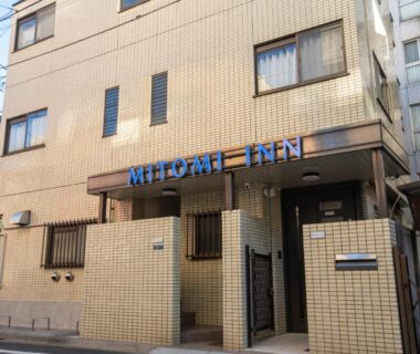 Beige tiled exterior and entrance of Mitomi Inn along a narrow Tokyo street