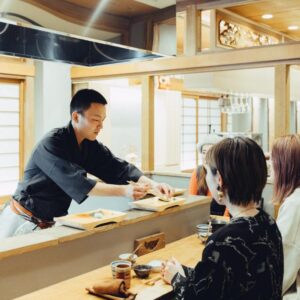 Chef serving guests at wooden counter with shoji screens in Mitsubikiya ryokan, Nagano, Chūbu region, Japan