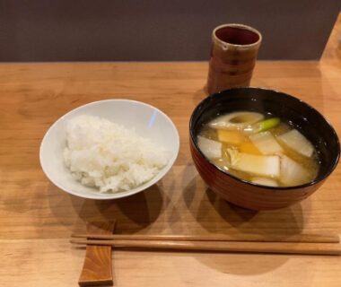 Steamed rice bowl, miso soup with tofu and scallions, chopsticks and ceramic cup on wooden table in Nagano