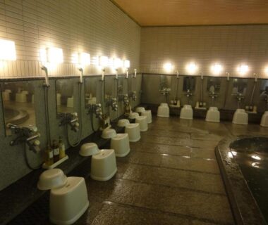 Row of wash stations and stools beside indoor bath at Miyajima Hotel Makoto, Chūgoku, Hiroshima, Japan