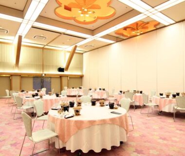 Spacious banquet hall with round tables, pink carpeting and ceiling lights at Miyajima Hotel Makoto in Hiroshima, Japan