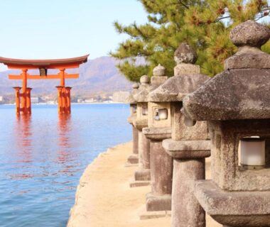 Red torii gate standing in shallow water with stone lanterns along the Miyajima shoreline