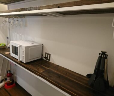 Microwave and hanging wine glasses on wooden kitchenette shelf at Miyajima Shiro Hiroshima
